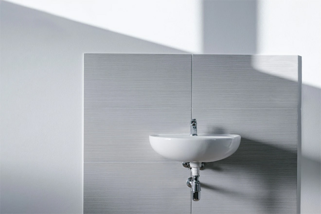 A white bathroom sink back by light grey wall tiles.