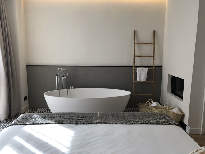 A bedroom with a freestanding bath. The wall behind is grey at the bottom and white on top