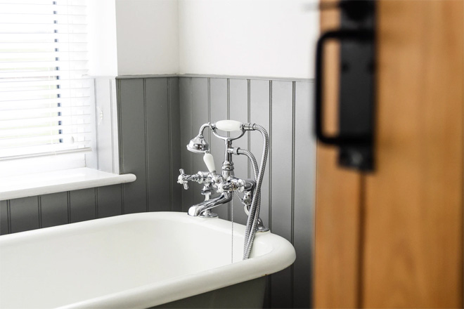 A white and grey freestanding bathtub with grey wooden panelling.