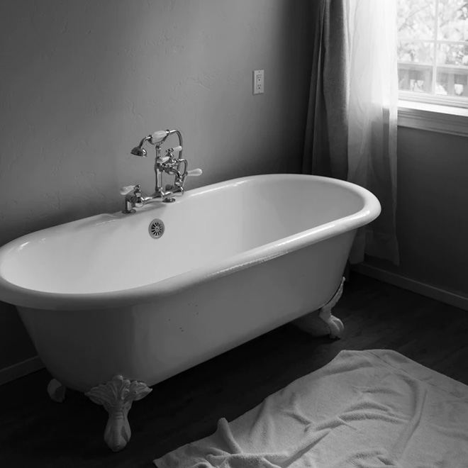 A white freestanding bath with a grey floor and painted grey walls