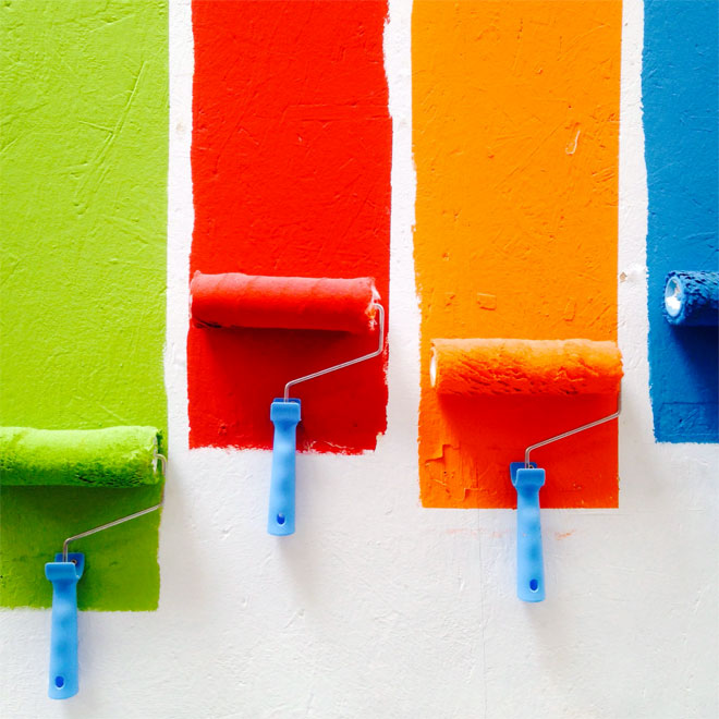 Some paint rollers applying different colours to a wall