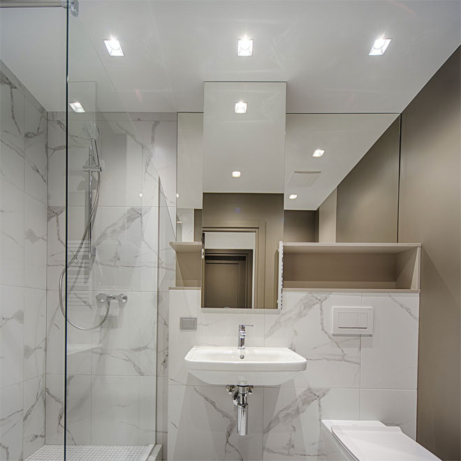 A white marble bathroom with recessed ceiling lights.