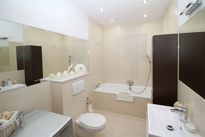 A cream and white windowless bathroom with bath, toilet and basin.